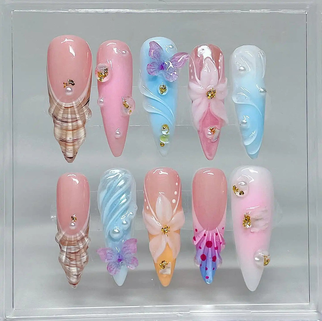 Handmade press-on nails with pastel butterfly, seashell, floral, and pearl designs on display
