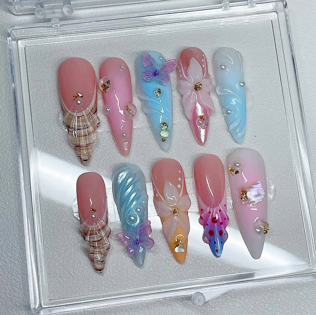 Handmade press-on nails with pastel butterfly, seashell, floral, and pearl designs on display