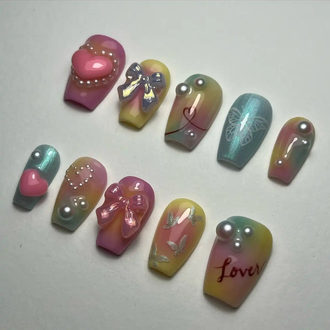 Handmade pastel iridescent press-on nails with 3D heart, bow, butterfly, pearls, and love designs.