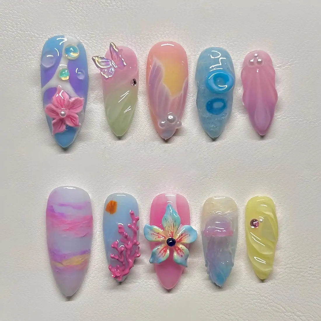 Handmade press-on nails with pastel ocean-themed designs, featuring flowers, coral, jellyfish, and seafoam accents.