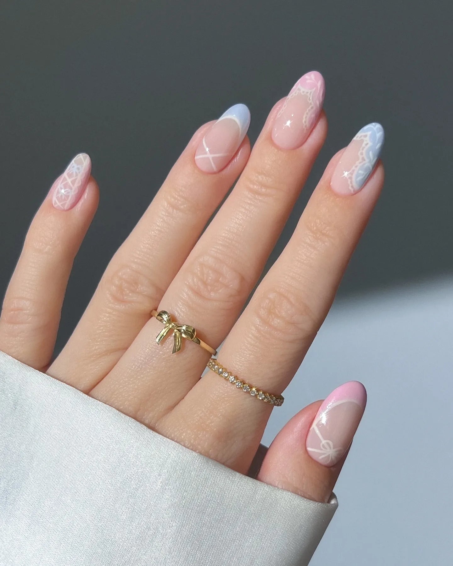 Hand with pastel pink and blue lace heart cottagecore press-on nails, gold rings visible.