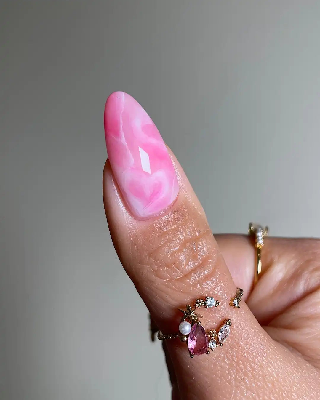 Hand with handmade pink marble jelly heart press-on nails in almond shape