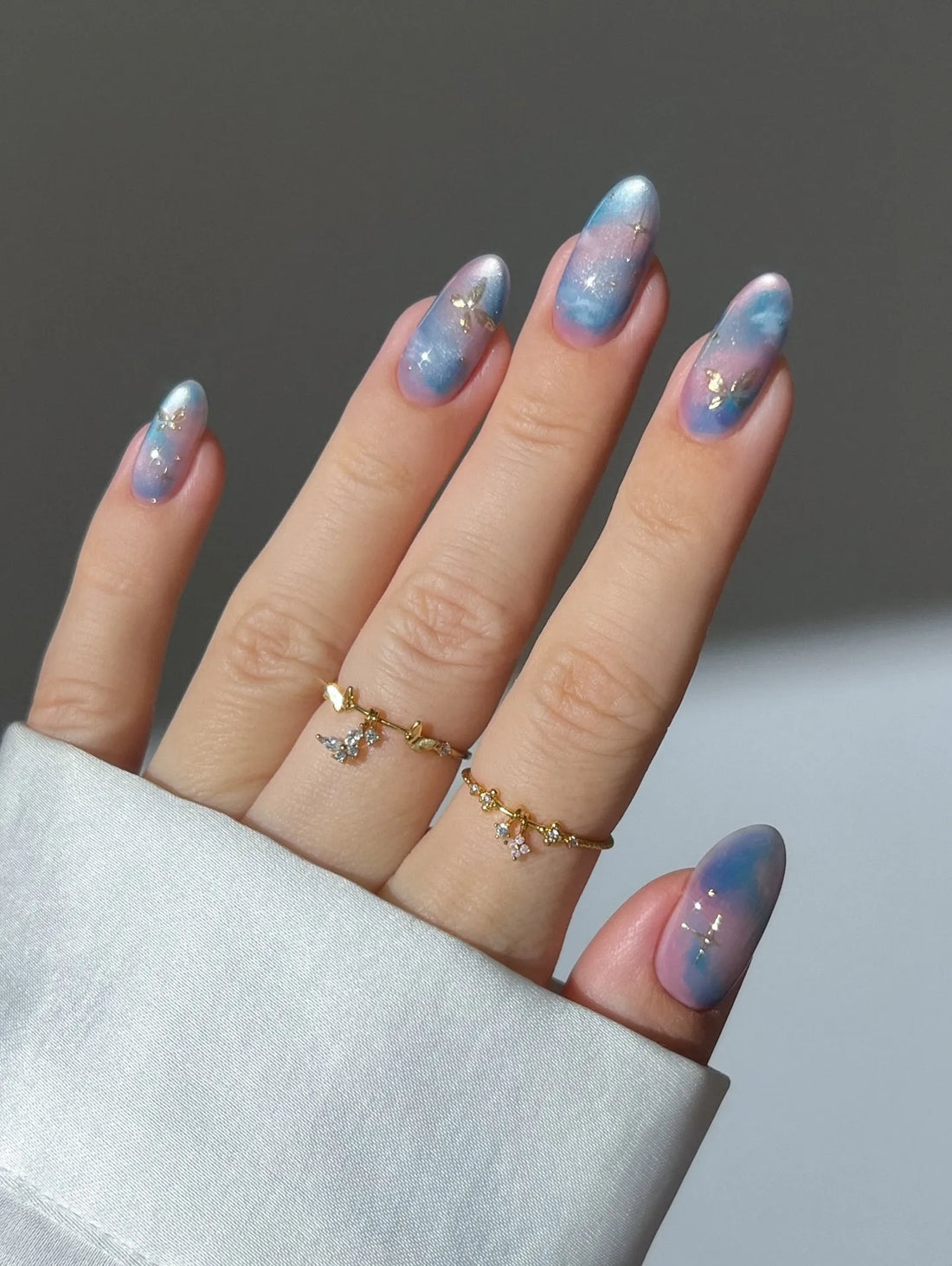 Hand with handmade ombre press-on nails in pink and blue with gold foil and galaxy accents