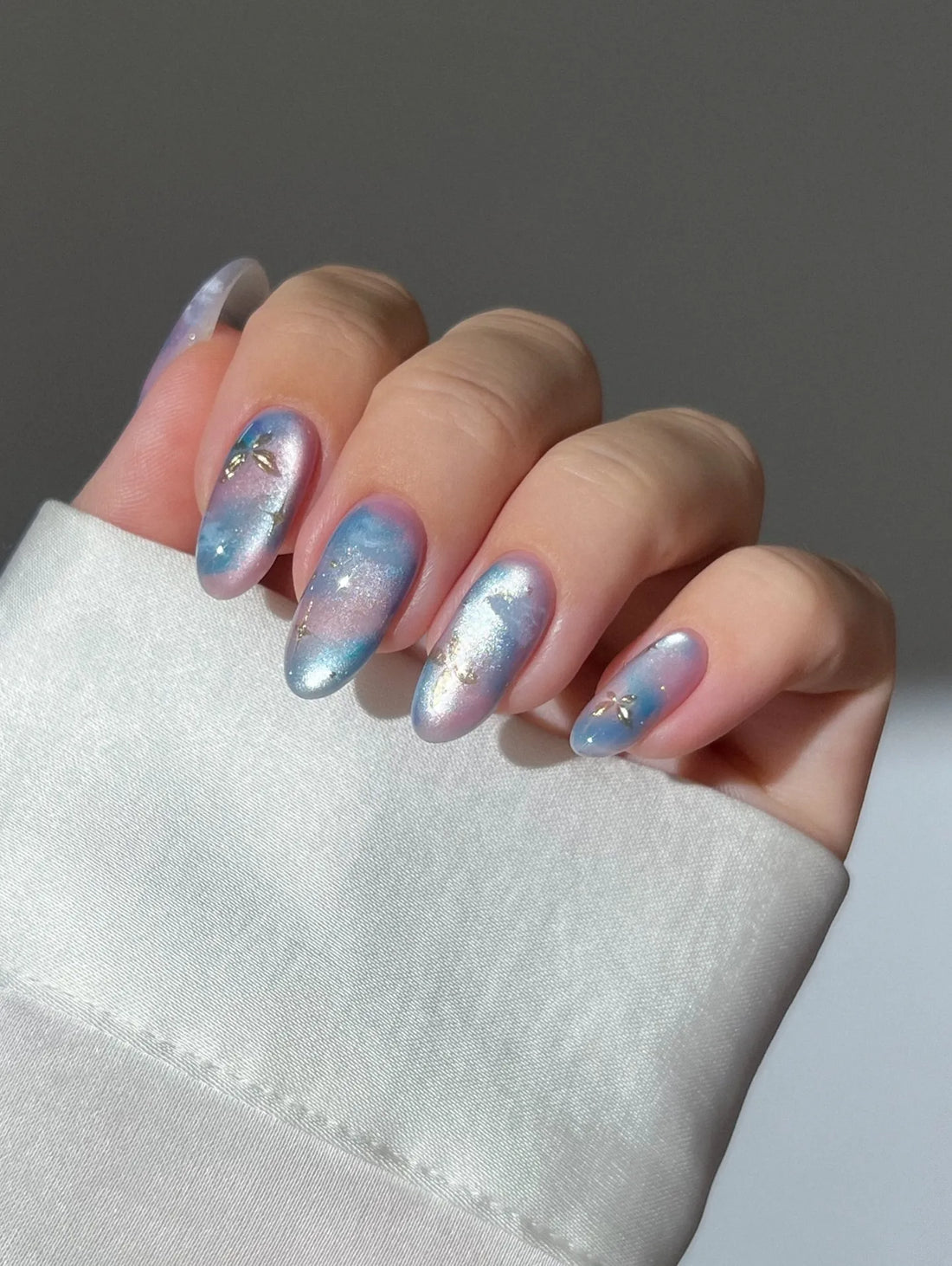 Hand with handmade ombre press-on nails in pink and blue with gold foil and galaxy accents