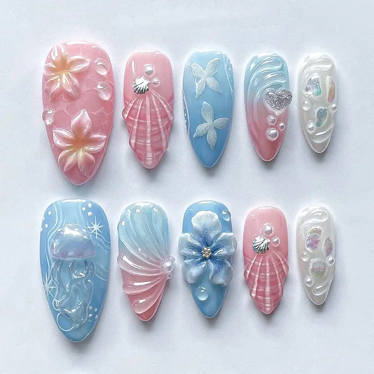 Handmade pink and blue press-on nails with seashell, jellyfish, floral, and mermaid designs.
