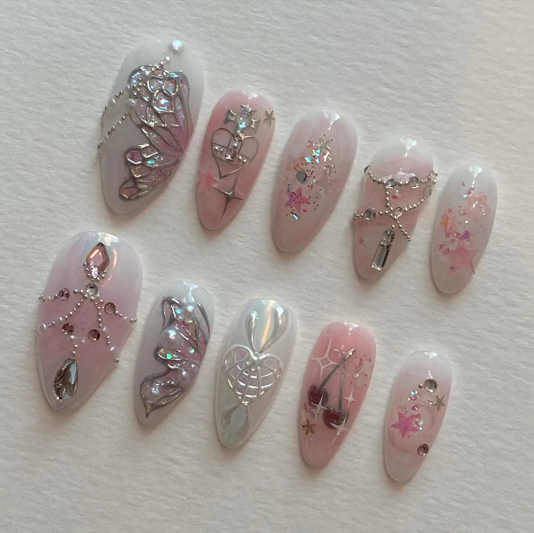 Handmade pink press-on nails with butterfly, heart, cherry, chain, and fairy designs