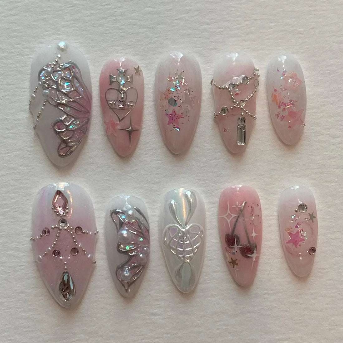 Handmade pink press-on nails with butterfly, heart, cherry, chain, and fairy designs