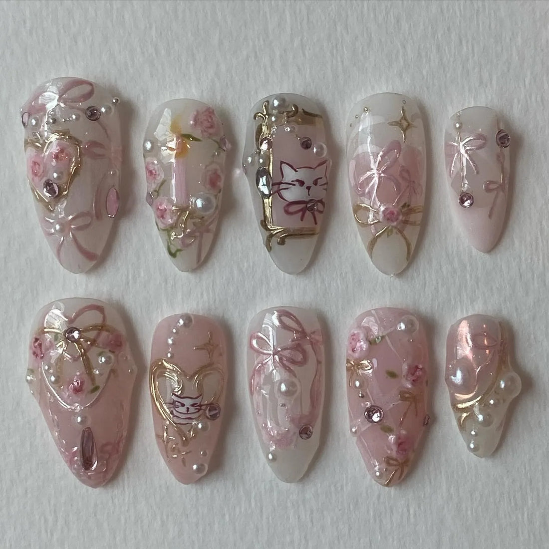 Handmade press-on nails with pink bows, cat design, roses, rose gold accents, and pearls.