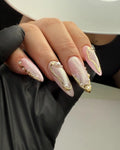 Hand with long pink shimmer press-on nails, gold accents, and 3D pearl designs