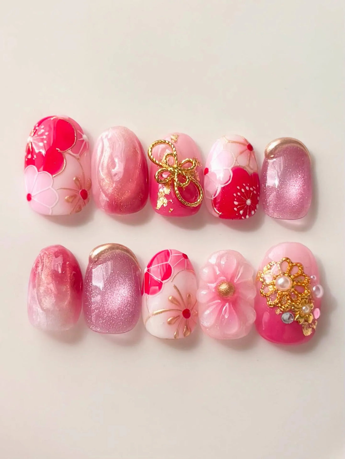Handmade pink press-on nails with cherry blossom designs, gold charms, and shimmer accents.