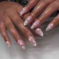 Hand with stiletto-shaped pink cherry blossom and silver glitter ombre press-on nails.