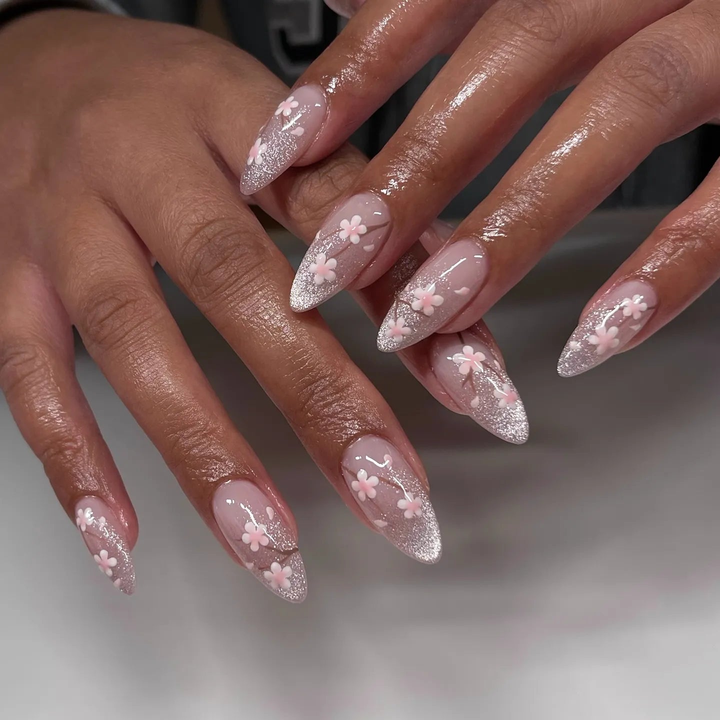 Hand with stiletto-shaped pink cherry blossom and silver glitter ombre press-on nails.