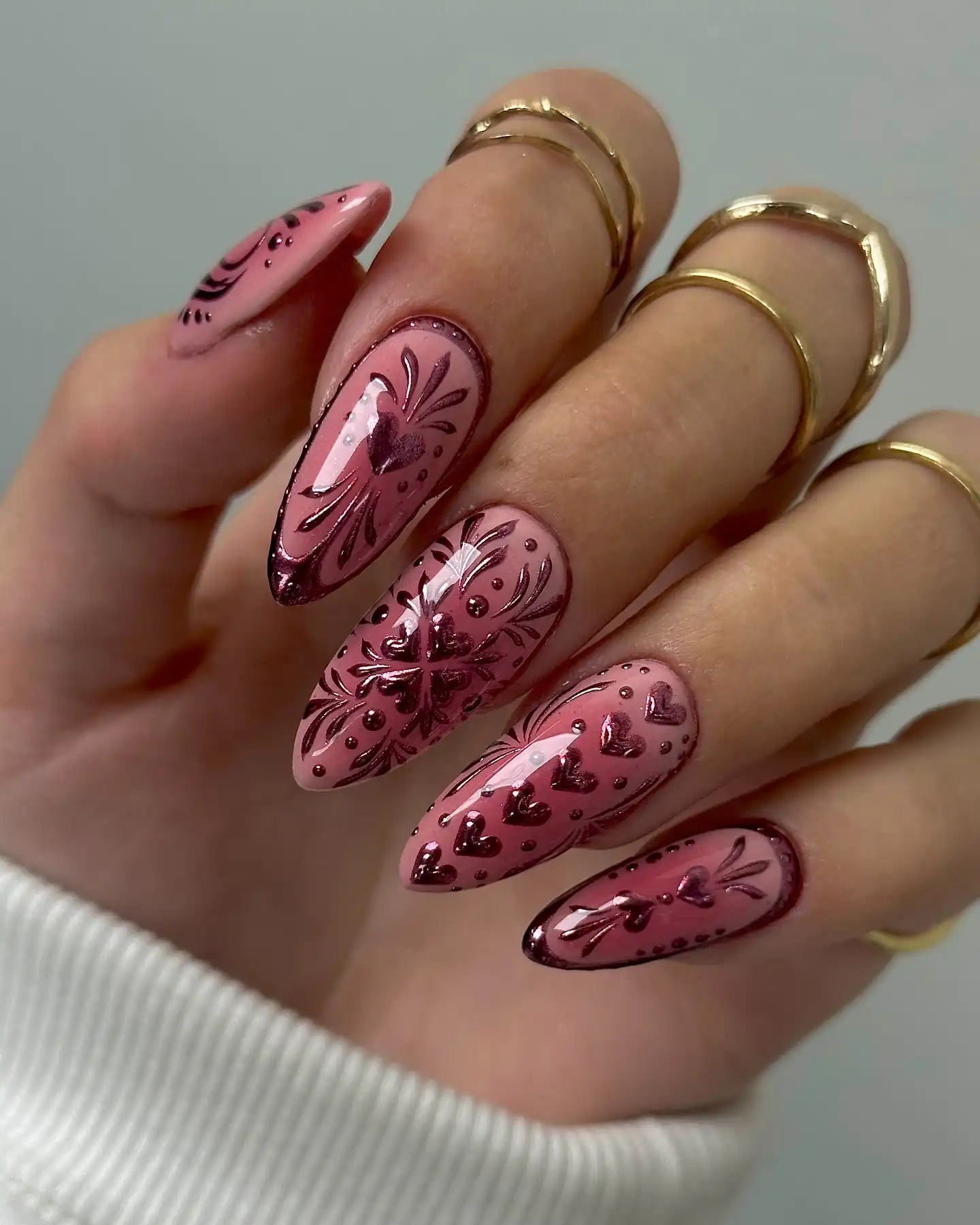 Hand showing long pink press-on nails with chrome heart and floral designs.
