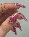 Hand holding handmade pink chrome press-on nails with heart and floral designs.