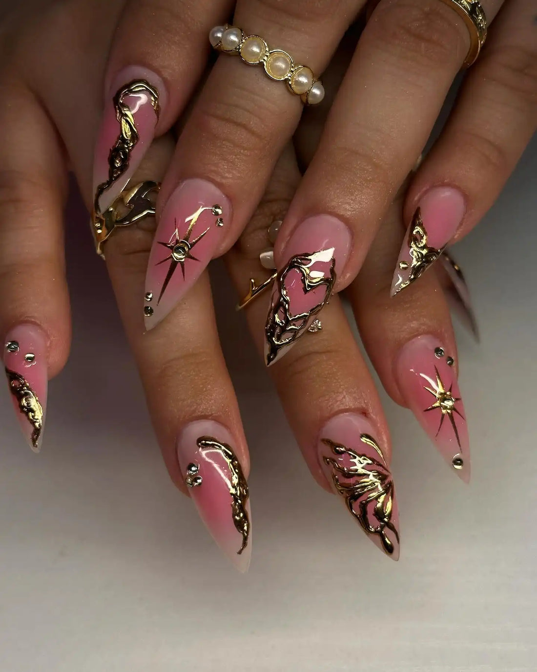 Handmade pink press-on nails with chrome heart and star designs, gold accents, and rhinestones.