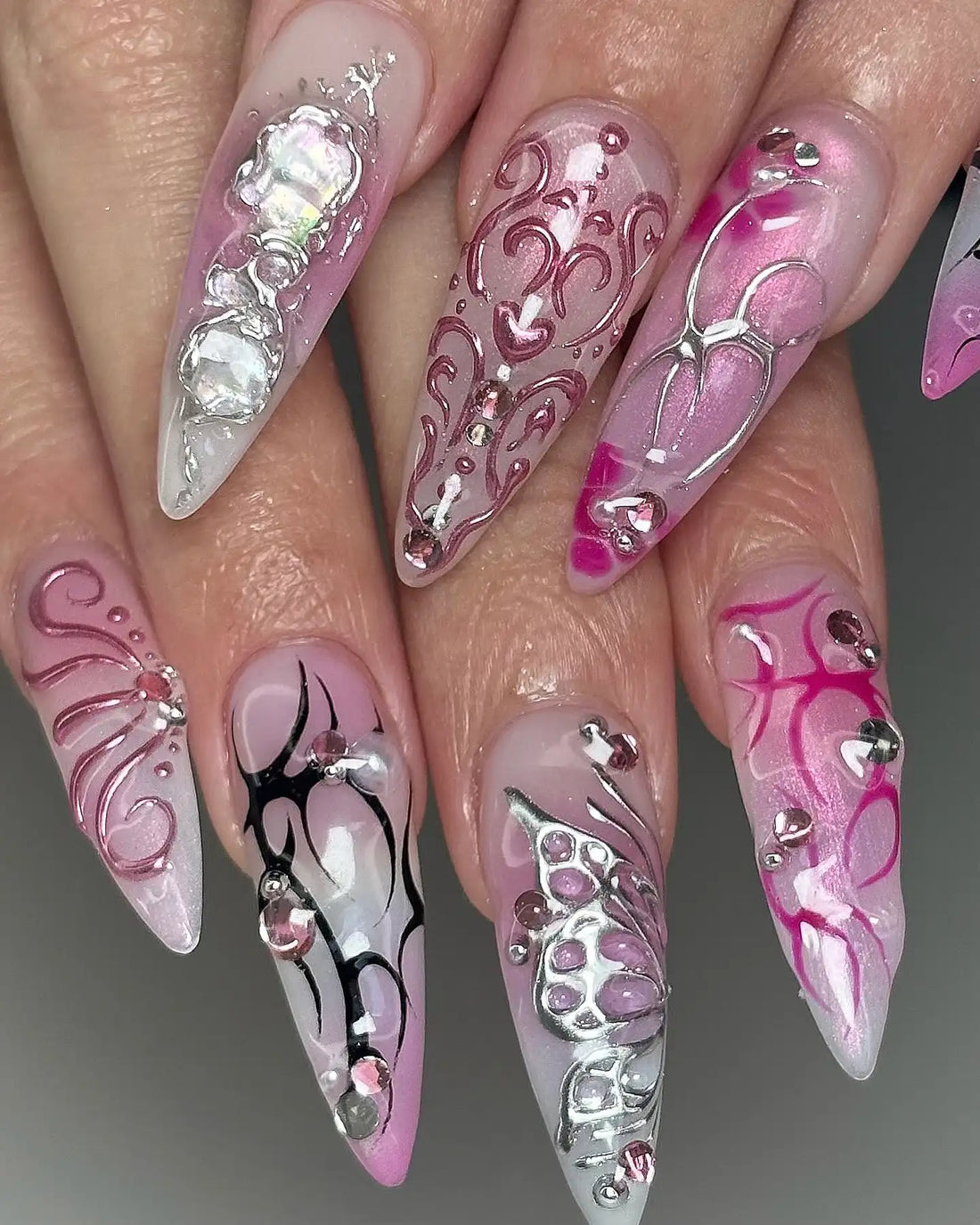 Hand with long stiletto press-on nails featuring pink, chrome, and silver rhinestone designs.