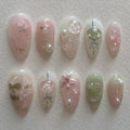 Handmade pink and green press-on nails with cherry blossom and pearl designs on a white background.