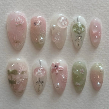Handmade pink and green press-on nails with cherry blossom and pearl designs on a white background.