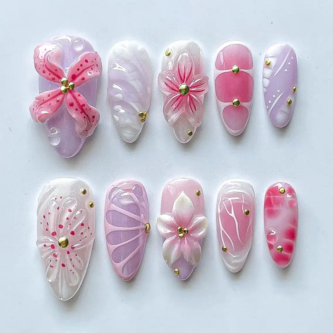Handmade pink and purple press-on nails with 3D flower designs and gold accents on white background.