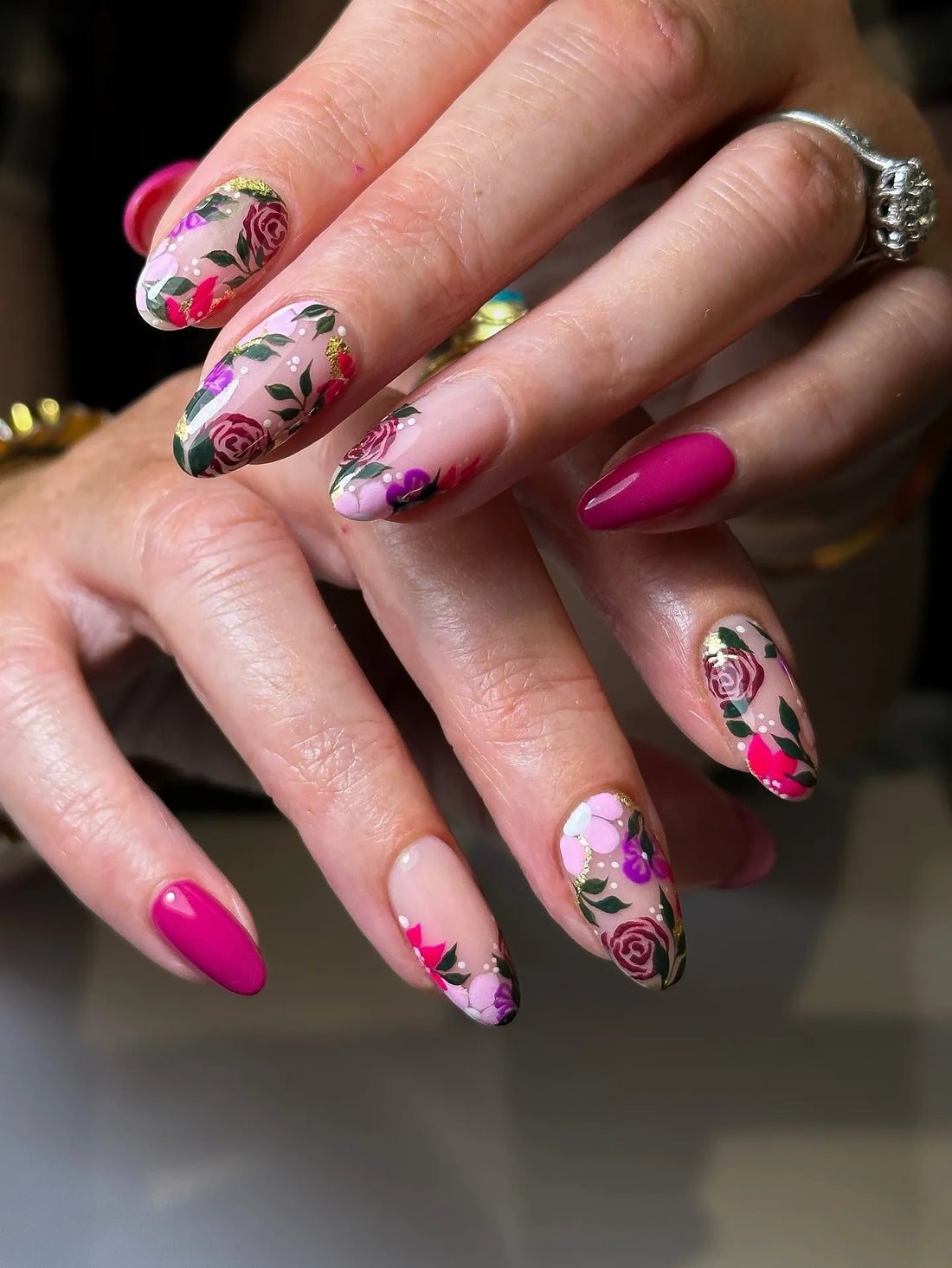Hand with pink and purple floral rose gold foil press-on nails, garden-inspired nail art.