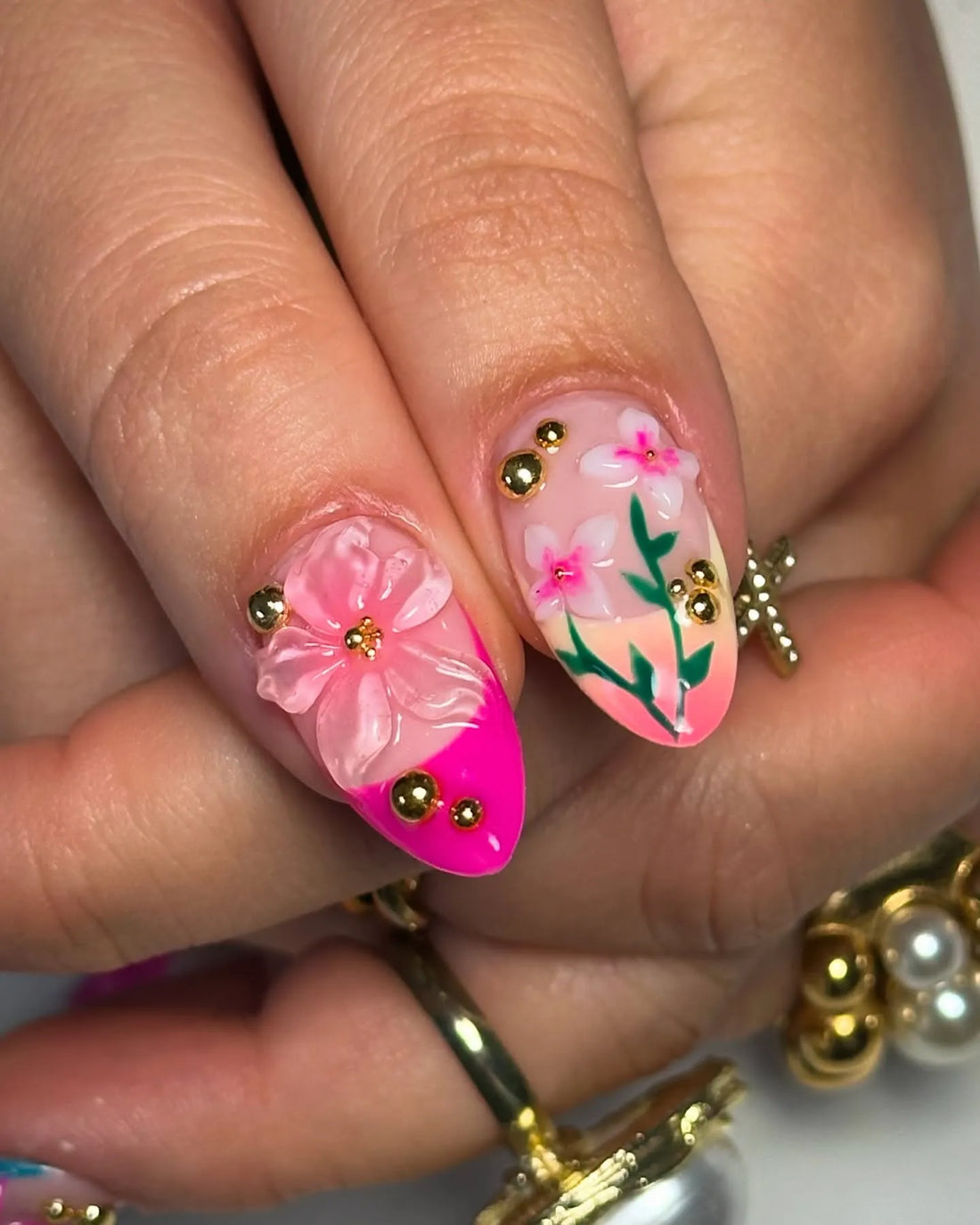 Hand with handmade pink, teal, green 3D floral press-on nails and gold accents.