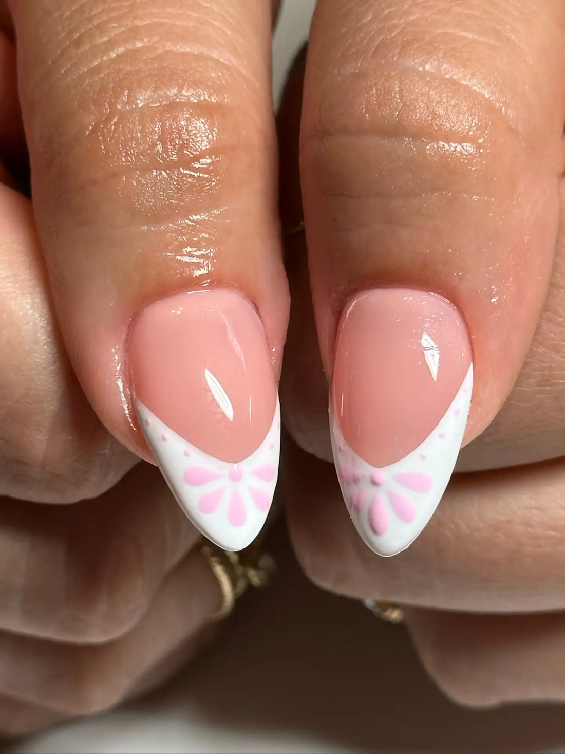 Hand with almond-shaped press-on nails featuring pink and white daisy flower French tips.