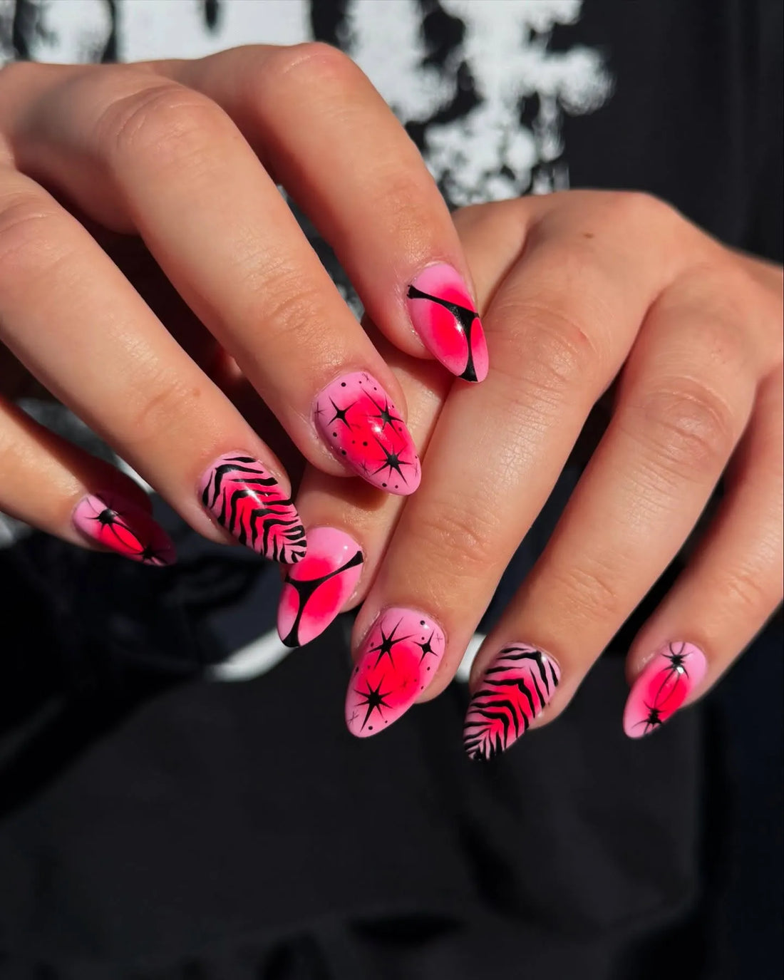 Hand with almond-shaped press-on nails, pink zebra and starburst designs, neon red accents.