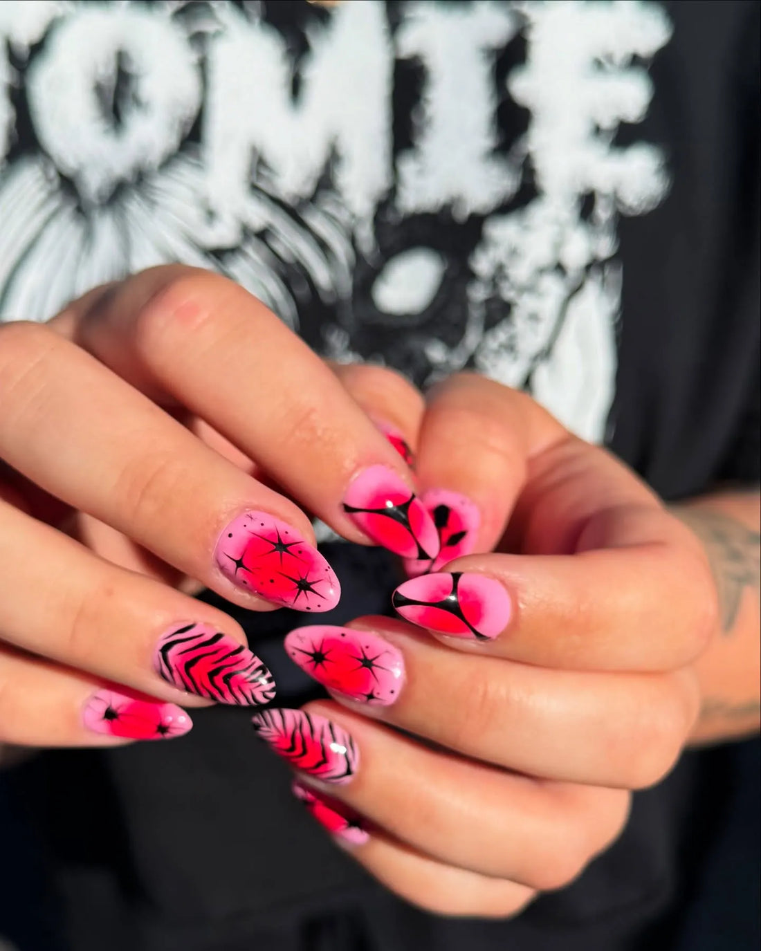 Hand with almond-shaped press-on nails, pink zebra and starburst designs, neon red accents.