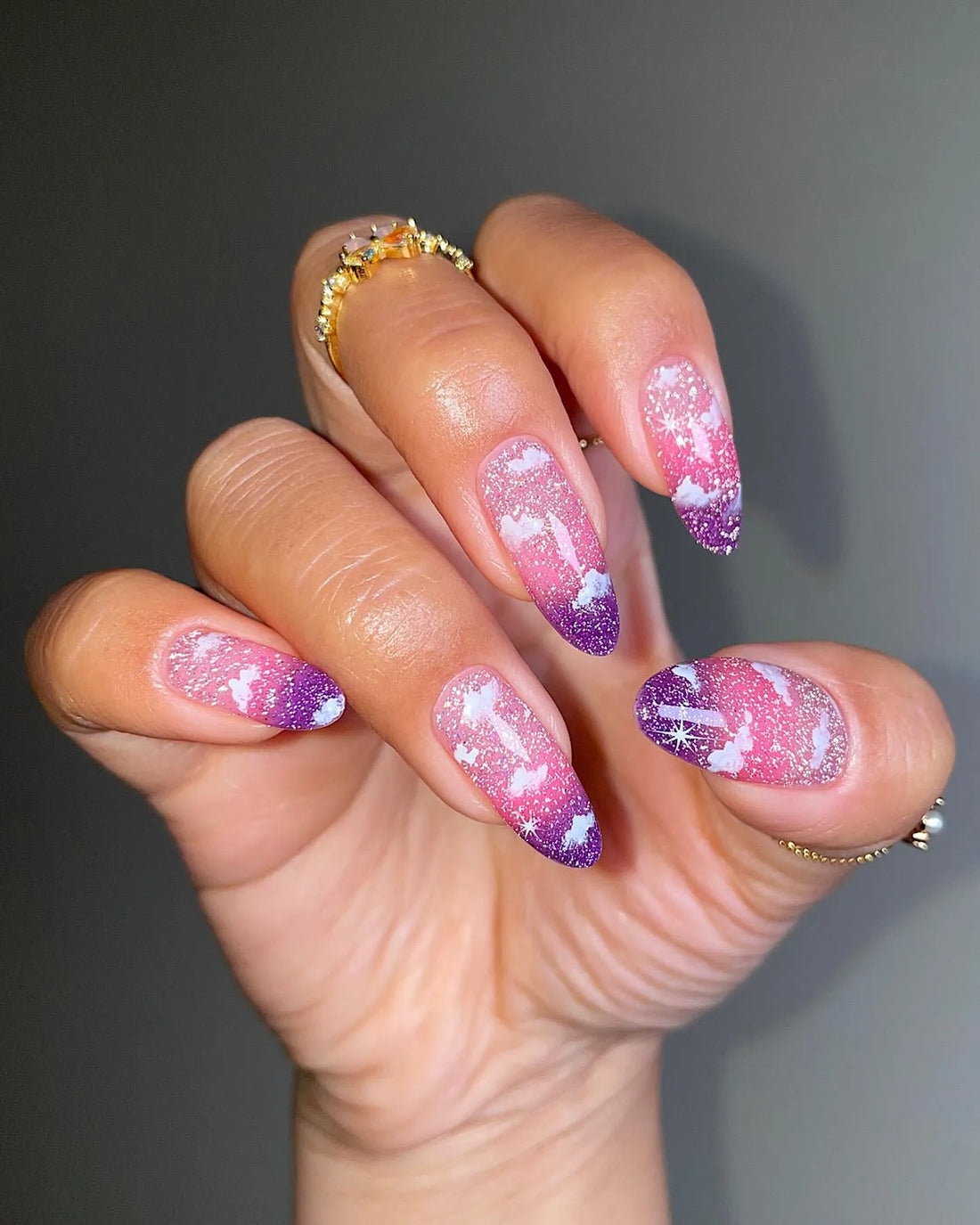 Hand with handmade pink and purple ombre press-on nails featuring cloud and glitter designs.