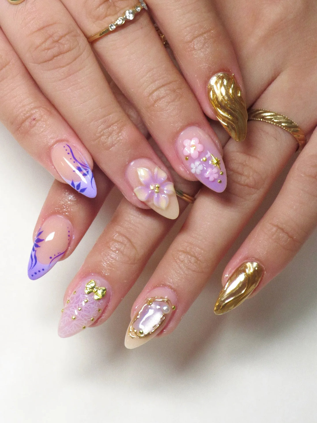 Handmade press-on nails with purple floral design, gold chrome accents, 3D flowers, and pearl details.
