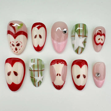 Handmade press-on nails with red apple, plaid green, and star designs, arranged on white background.