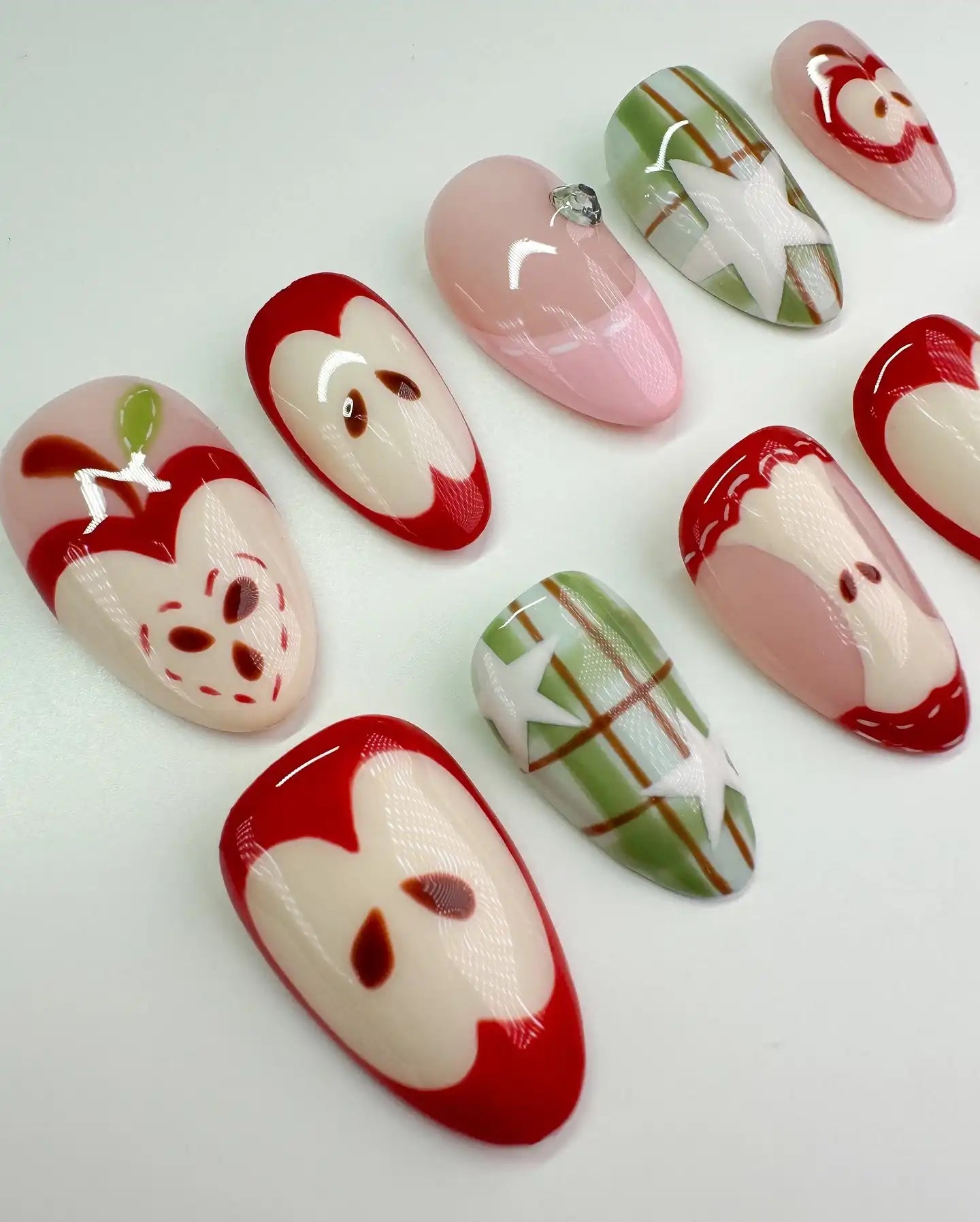 Handmade press-on nails with red apple fruit and green plaid designs on white background.