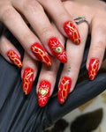Handmade red press-on nails with gold chain, starburst, and golden heart designs.