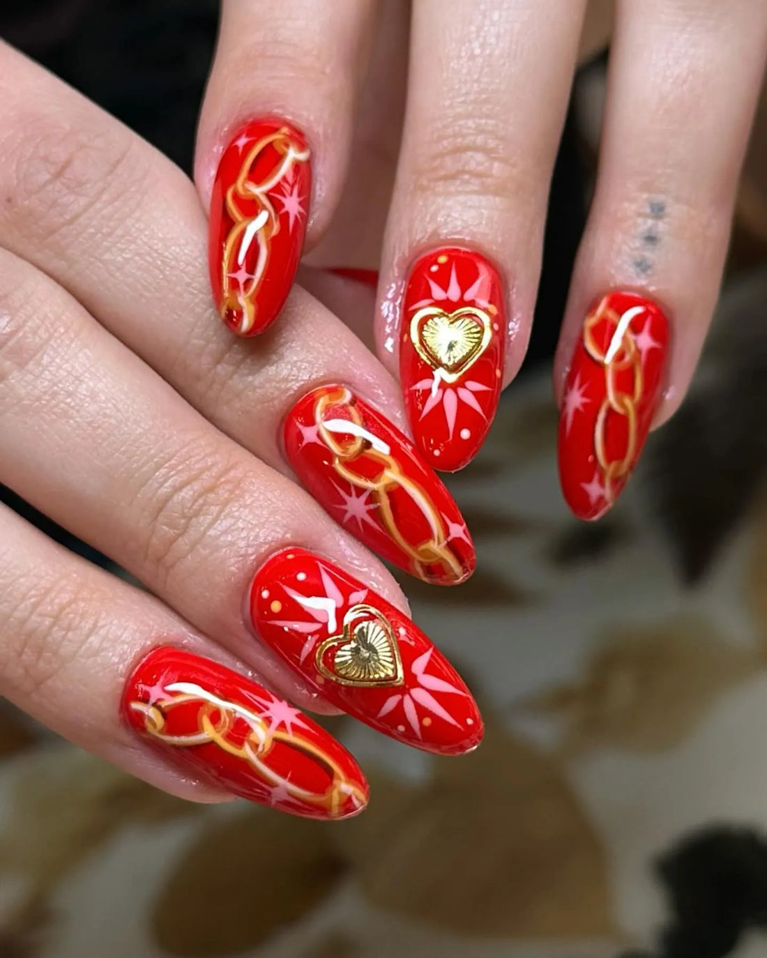 Handmade red press-on nails with gold chain, starburst, and golden heart designs.