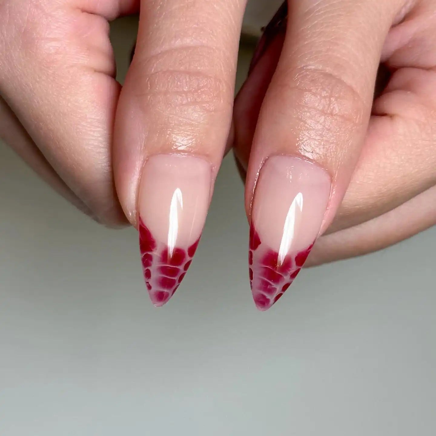 Handmade press-on nails with red snakeskin tip design on almond-shaped nails.