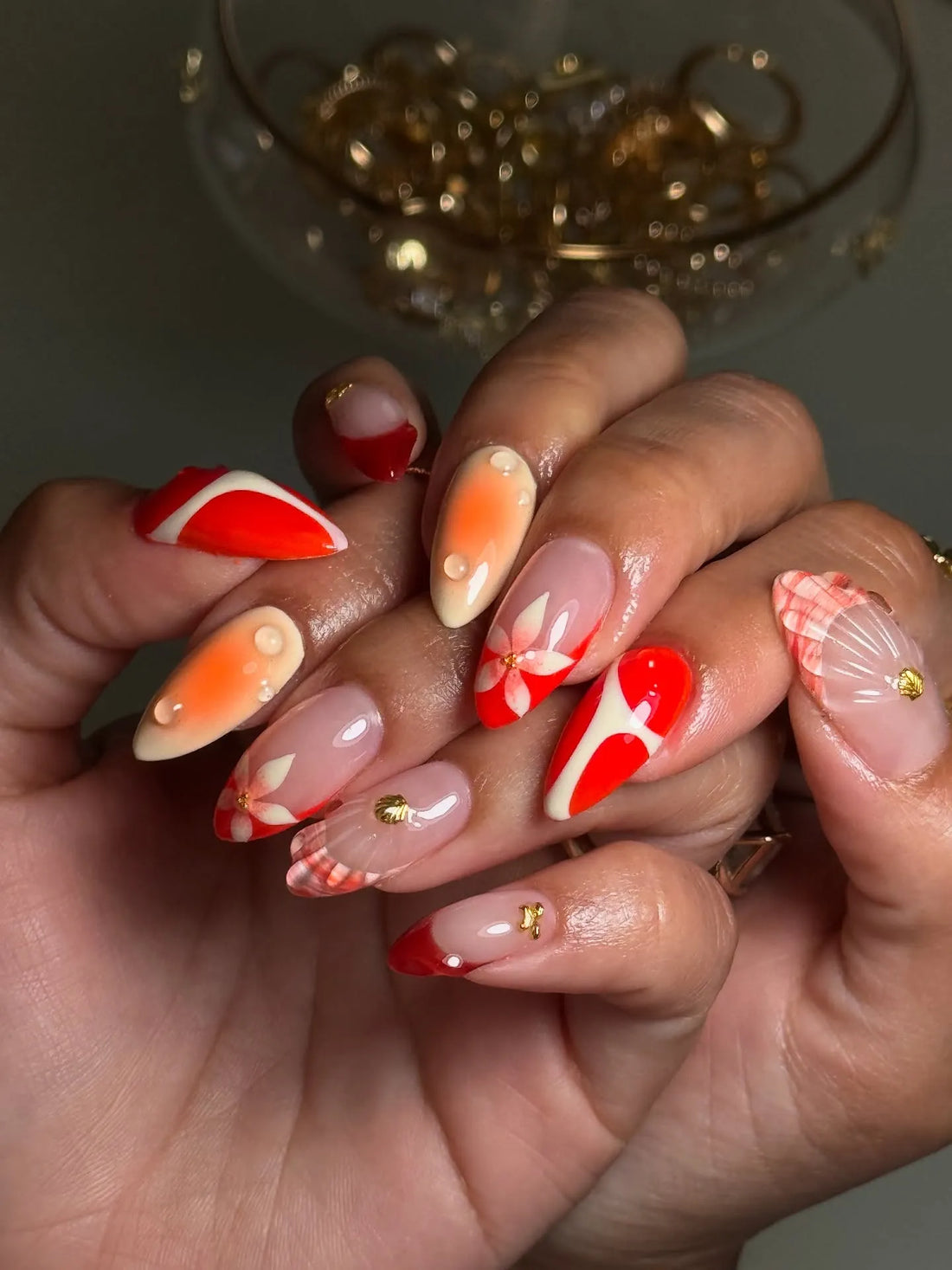 Hand with handmade red floral tropical press-on nails featuring shell and gold accents