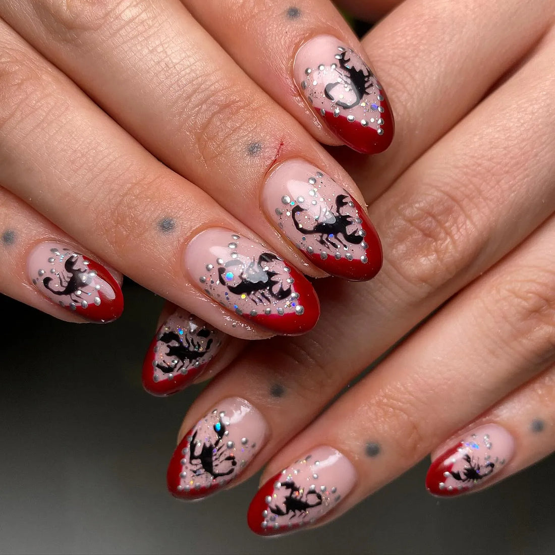 Handmade press-on nails with red French tips, black scorpion art, and silver glitter accents.