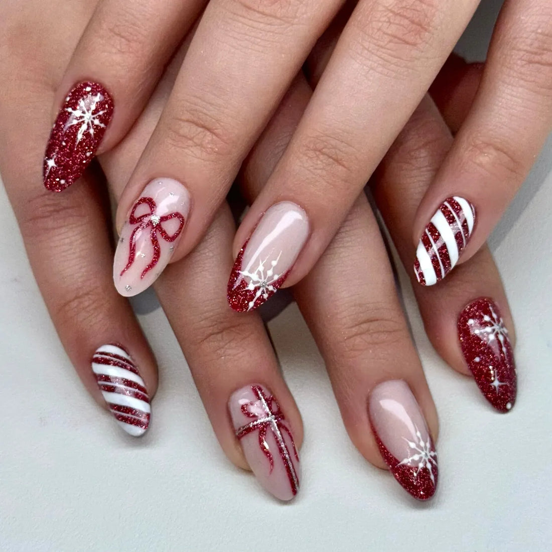 Handmade red glitter press-on nails with stripe, bow, and snowflake holiday designs