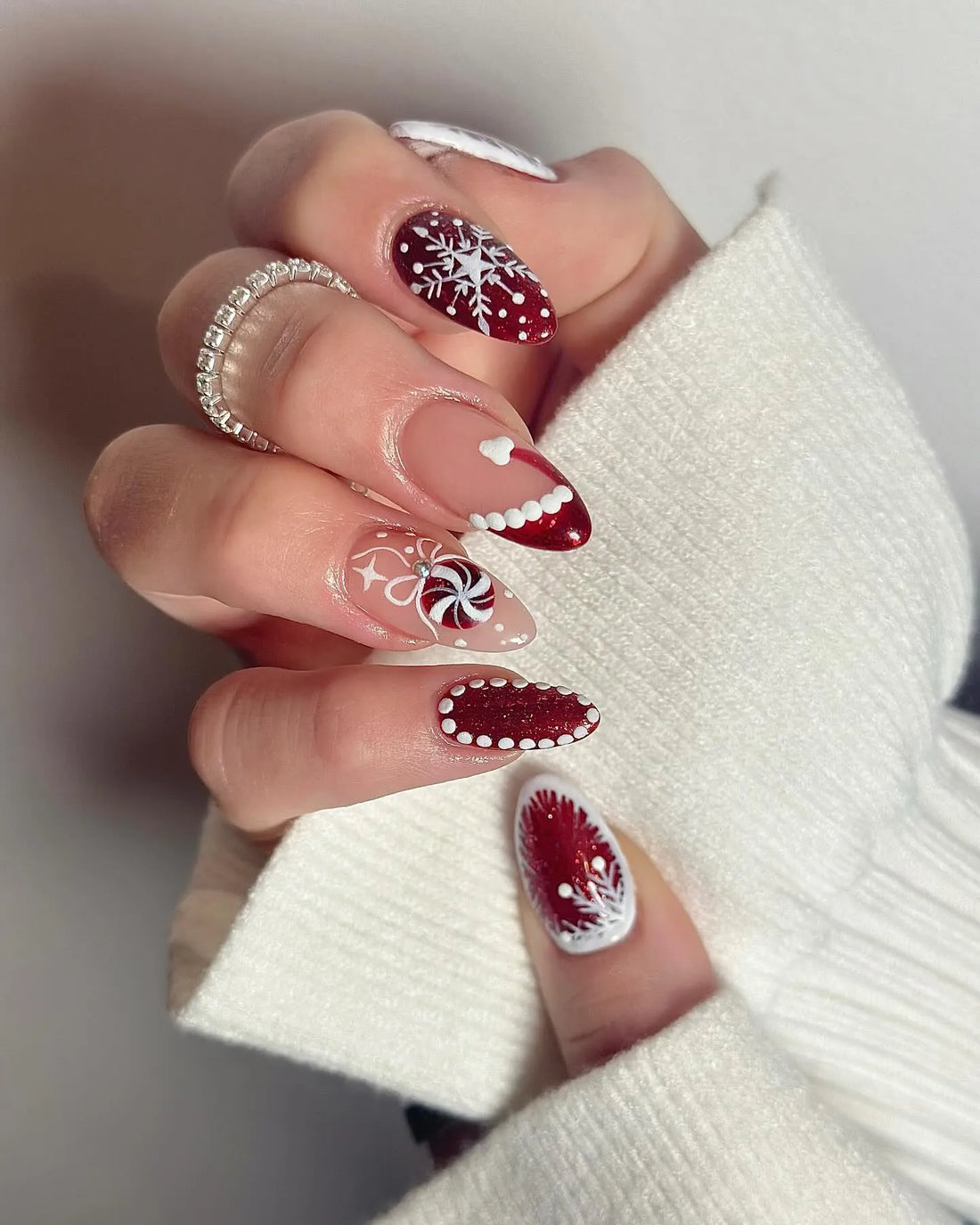 Hand wearing red and white glitter winter press-on nails with snowflake and candy cane designs