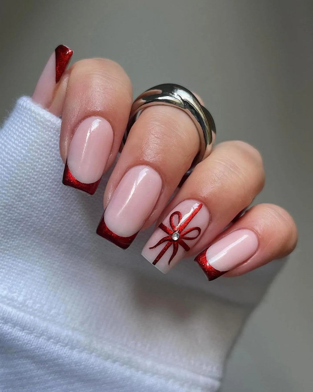 Hand with handmade red glitter French tip press-on nails, one nail with ribbon design