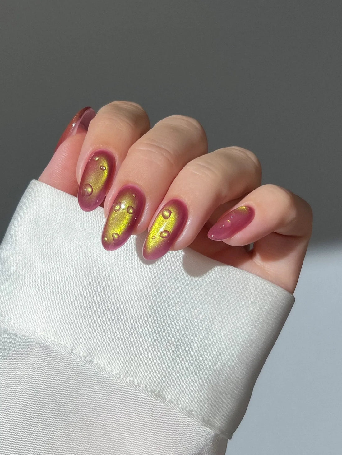 Hand wearing handmade red and gold chrome cat eye press-on nails with water drop effect.