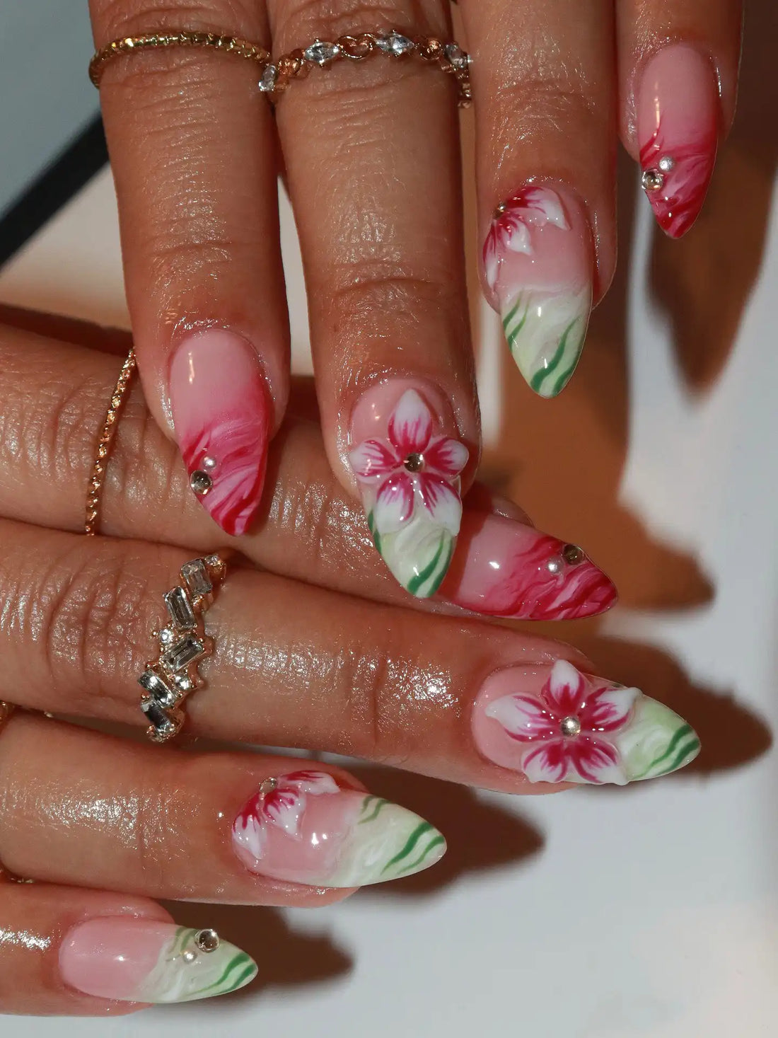 Hand with long press-on nails featuring handmade red hibiscus flower and green accents.