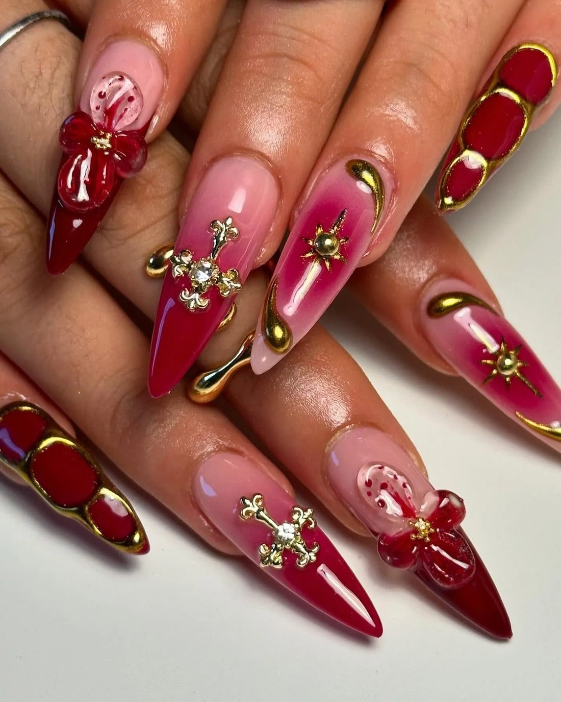 Handmade red and pink press-on nails with 3D floral, cross, celestial gold accents, almond shape
