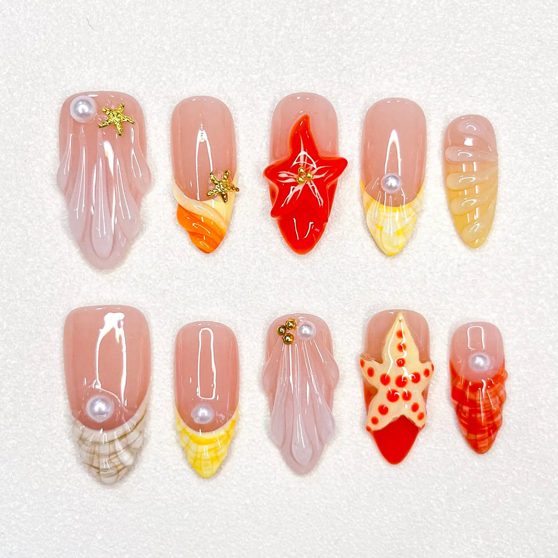 Handmade press-on nails with red starfish, seashell, and pearl beach designs on white background