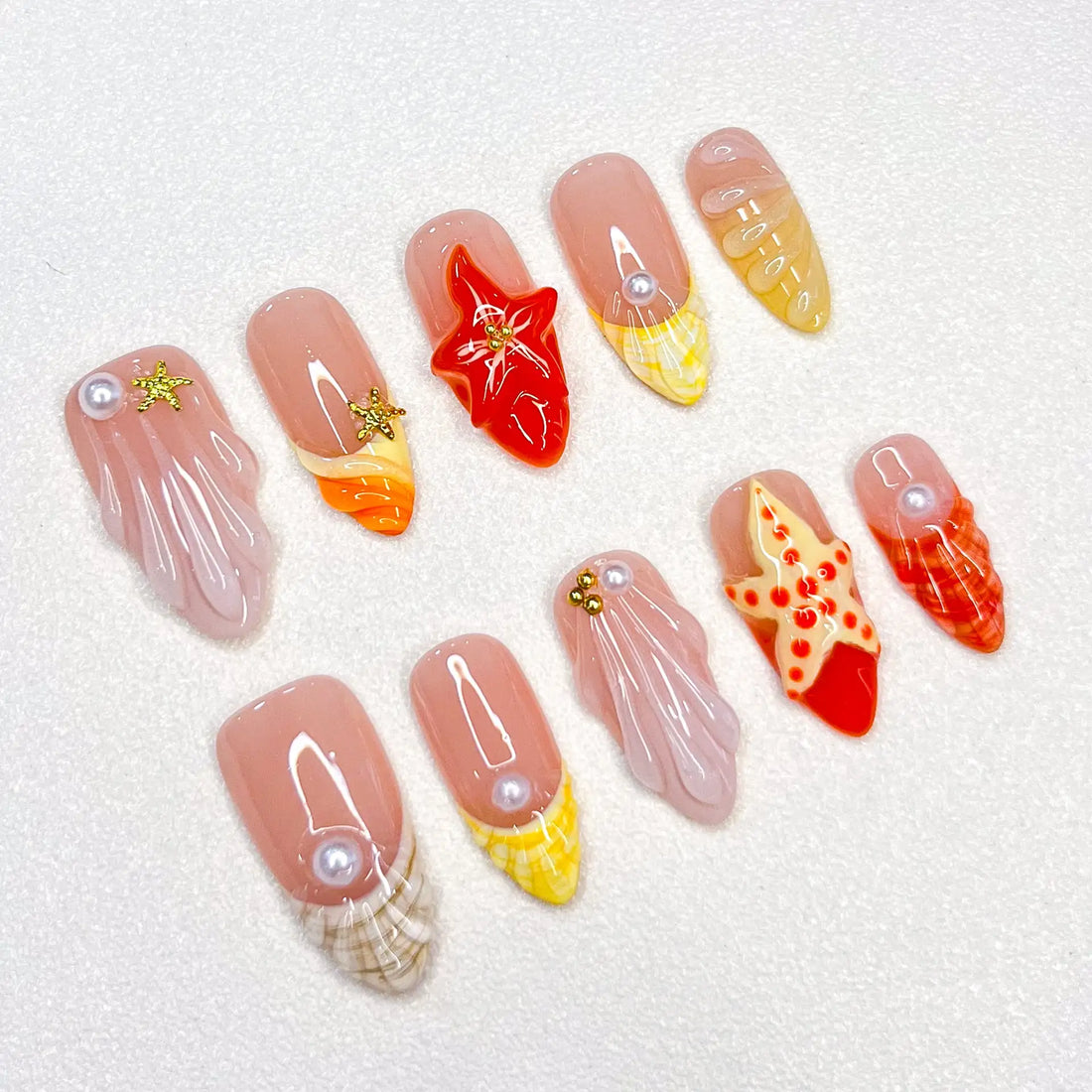 Handmade press-on nails with red starfish, seashell, and pearl beach designs on white background