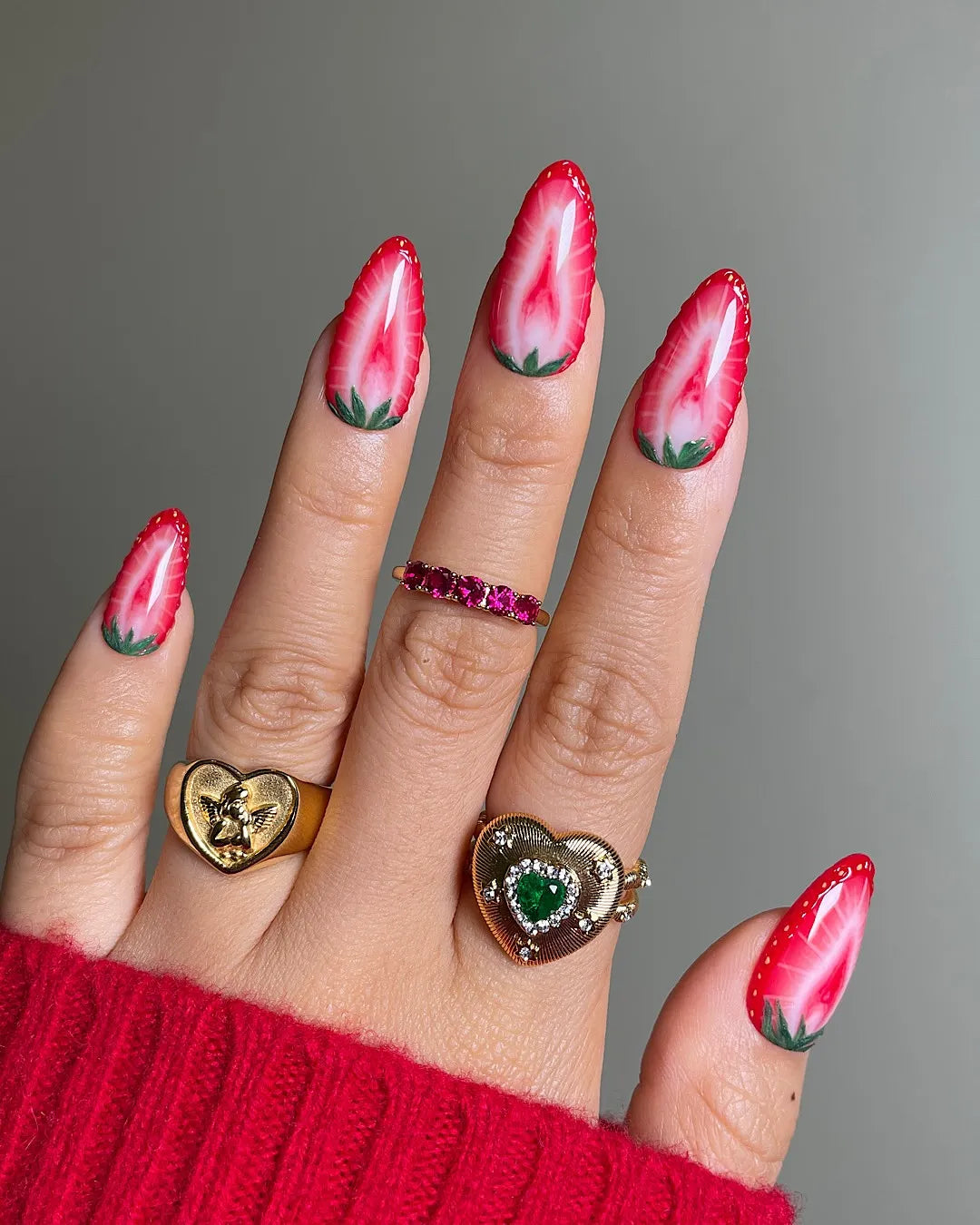 Hand holding summer fruit-themed handmade press-on nails with realistic strawberry art design.