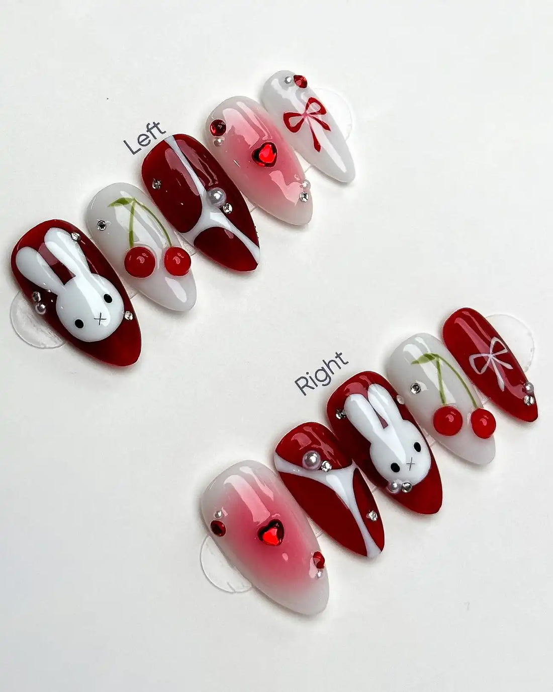 Handmade red and white press-on nails with bunny, cherry, bow, and heart designs.