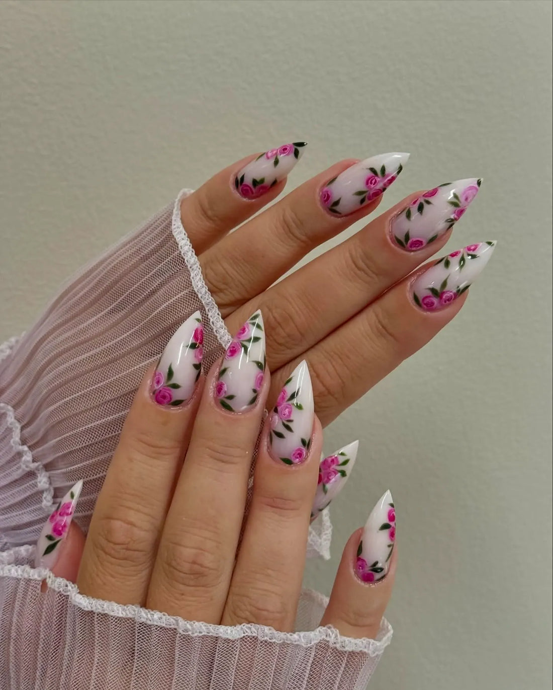 Hand with long stiletto press-on nails featuring hot pink rose floral design