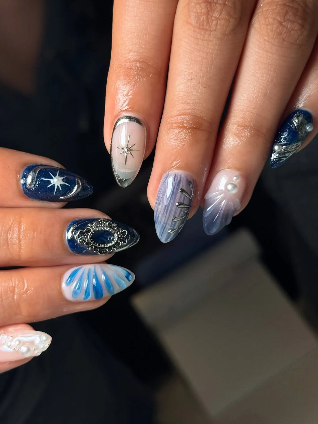 Hand with royal blue shimmer press-on nails featuring 3D pearl charms and starburst designs.