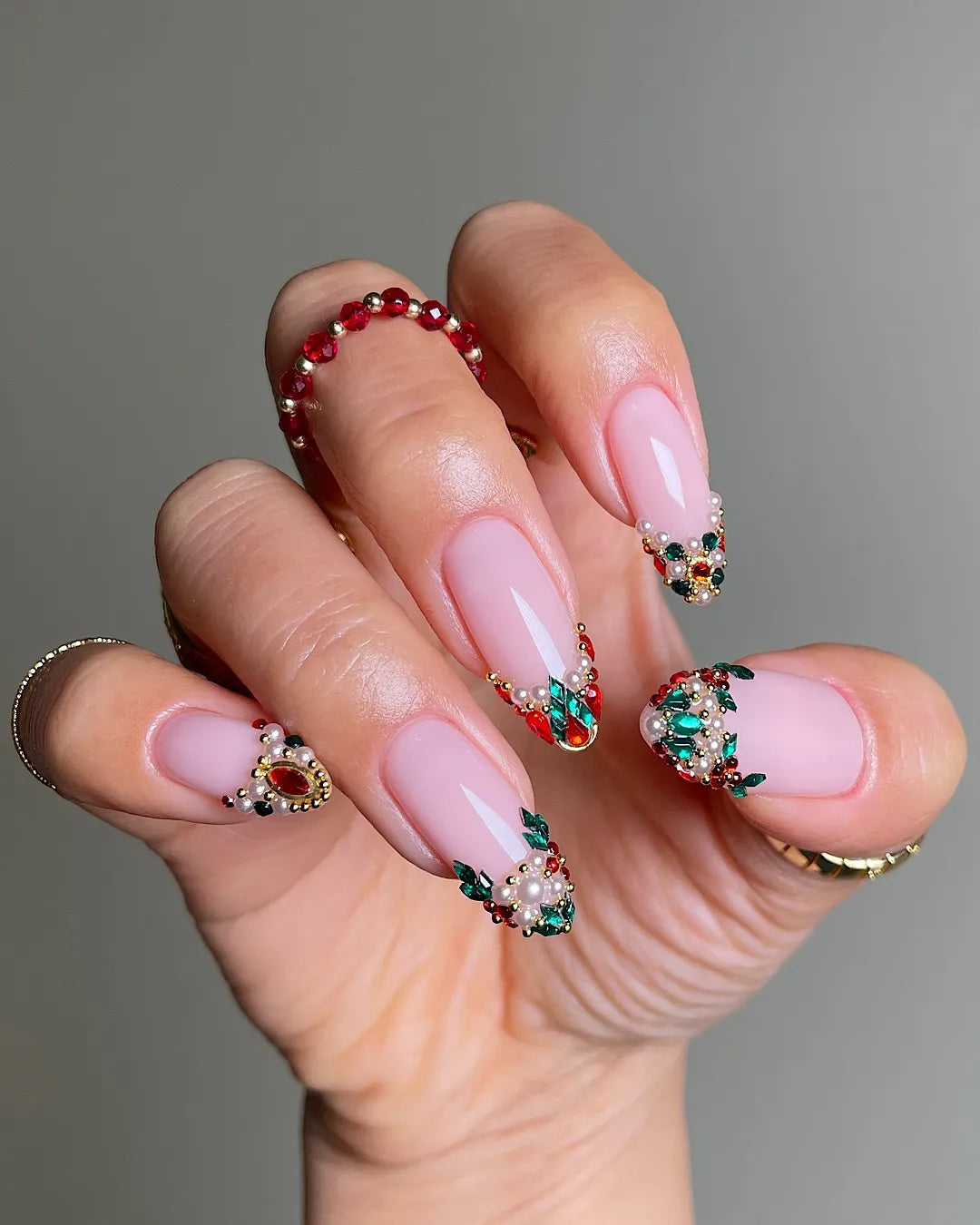 Hand with handmade press-on nails featuring ruby, emerald, and pearl French tips, festive design.